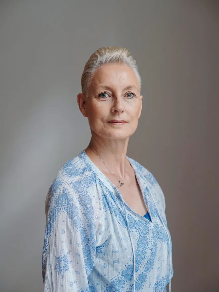 Patricia Thielemann mit kurzen hellen Haaren in einer hellblau gemusterten Bluse, ruhiger Blick in die Kamera.